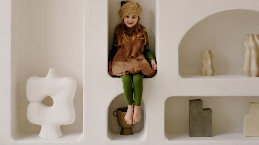 little girl sitting on shelf surrounded by sculptures
